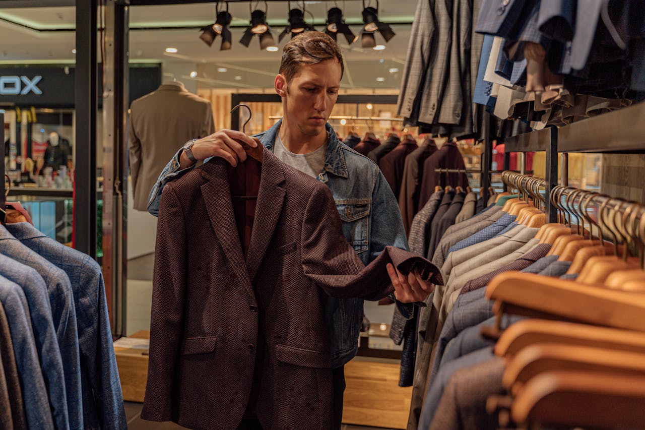 about-us-02 Man browsing stylish blazers in a modern clothing store, considering fashion options.