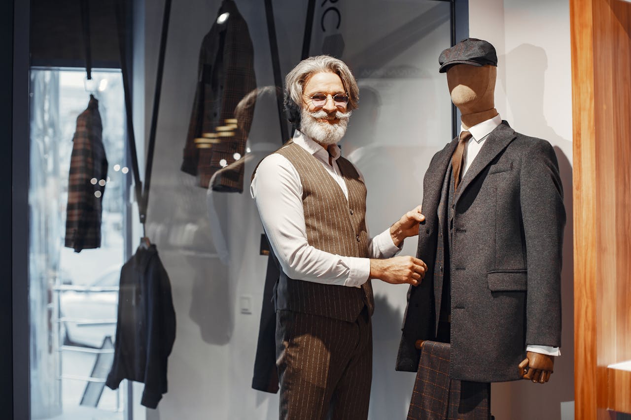 services-01 Elegant senior man in tailored vest styling a mannequin in designer menswear inside a fashion boutique.